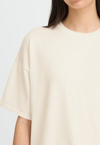 T-shirt surdimensionné de couleur crème avec un col rond et des manches courtes, présentant une texture douce et lisse ainsi qu'une coupe décontractée.