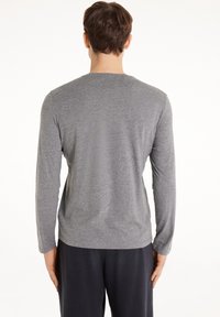 Šedá dlouhá rukávová košile vyrobená z měkkého materiálu, s kulatým výstřihem a volným střihem. Jednoduchý design bez výrazných vzorů nebo akcentů.