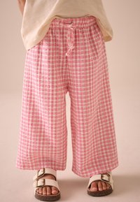 Pantaloni roz cu model în carouri, cu croială largă, dintr-un material ușor, având talie elastică și șnur; asortați cu sandale albe.