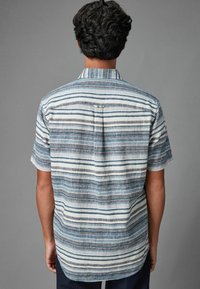 Koszula z krótkim rękawem z lekkiego materiału, z poziomymi paskami w kolorach niebieskim, szarym i białym. Plecy mają subtelna kieszeń oraz zaokrąglony dół.