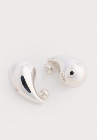 Srebrne kolczyki w kształcie łezki z wypolerowanymi powierzchniami i zapięciami na szpilki. Posiadają gładkie krzywizny oraz mały czarny akcent na jednym z nich.