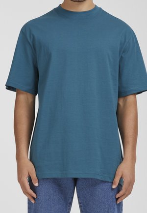 Krótka koszulka z krótkim rękawem w kolorze morskim z okrągłym dekoltem, wykonana z bawełnianej tkaniny. Charakteryzuje się luźnym krojem i minimalnymi detalami szwów.