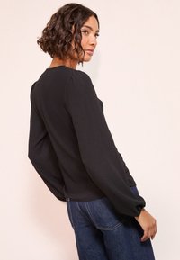 Černý ribovaný top s dlouhým rukávem a nafouklými rameny, měkká textura a přiléhavý střih. Kombinováno s modrými džínami s vysokým pasem.