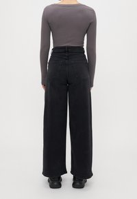 Svarta vida jeans med hög midja, med en femfickdesig och en slät textur. Kompletteras av en åtsittande grå långärmad topp.