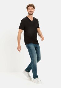 Zwarte v-hals t-shirt in combinatie met blauwe spijkerbroek en witte sneakers. Het shirt heeft korte mouwen en een gladde textuur.