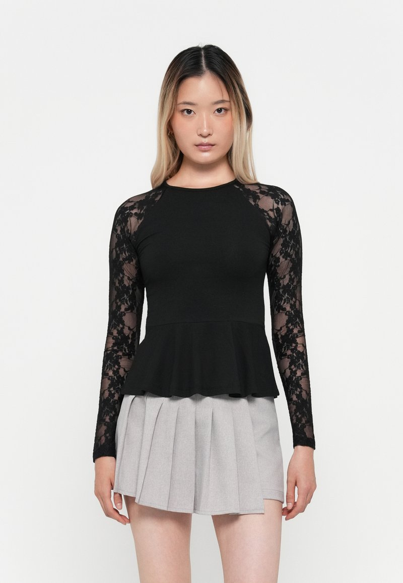 Black long-sleeve top with lace sleeves, peplum hem, paired with a light gray pleated skirt. Simple design with contrasting textures.