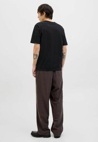 Svart t-shirt med korta ärmar i kombination med brun rutig byxa; synliga tatueringar på armarna; mjukt tyg och avslappnad passform.