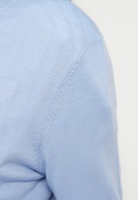 Ανοιχτό μπλε πλεκτό πουλόβερ με λεία υφή, ριγέ μανσέτες και ραφή στον ώμο, που παρουσιάζει απλές και καθαρές γραμμές.