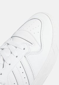 Vit sneaker med ett glatt läderfoder, perforerat tåparti och ton-i-ton-sömmar. Har vita snören och en texturerad gummisula.