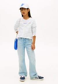 Λευκό τοπ με κοντά μανίκια κάτω από ένα ανοιχτό μπλε καρό ζακέτα, συνδυασμένο με ανοιχτό μπλε καμπάνες τζιν και ναυτικό μπλε αθλητικά παπούτσια. Κρατάει μια μικρή μπλε τσάντα.