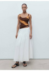 Brown and orange striped ribbed tank top paired with a white, flowy, ankle-length skirt. Model wears black flat sandals. Smooth texture.