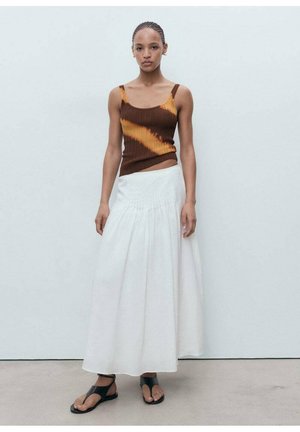 Braun und orange gestreifter gerippter Tanktop, kombiniert mit einem weißen, fließenden, knöchellangen Rock. Das Model trägt schwarze flache Sandalen. Glatte Textur.
