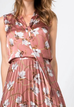 Ensemble composé d'un chemisier rose sans manches et d'une jupe plissée, avec des motifs floraux blancs et des chaînes dorées sur un fond clair.