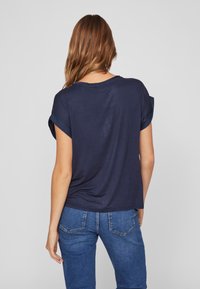 Námořnická modrá tričko s krátkým rukávem a ohrnutými rukávy, volného střihu, vyrobené z měkké tkaniny, v kombinaci se světlými modrými džíny.