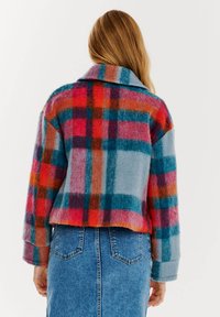 Károvaná bunda v modrých, červených a oranžových odtieňoch, s širokým golierom a skráteným strihom, s jemným, textúrovaným povrchom.