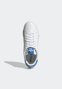 White leather sneaker with lace-up closure, blue padded tongue, and perforated side details. Features branding on tongue and inner sole.