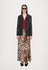 Blazer in pelle nera sopra un cardigan rosso con bottoni e perle, abbinato a una gonna maxi in stampa leopardata e scarpe nere con tacco.