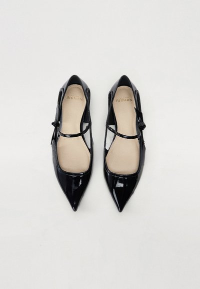 Ballerines en cuir verni noir avec un bout pointu, des côtés découpés et un nœud décoratif. L'int�érieur présente une semelle beige avec une marque.