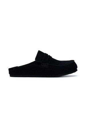 Mocasín negro sin cordones con una tira de velcro en la parte superior y una suela texturizada, mostrado de lado sobre un fondo blanco.
