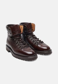 Scarponi da trekking in pelle marrone con finitura texturizzata, occhielli in metallo e linguetta marrone a contrasto. Suola in gomma robusta e sistema di allacciatura.