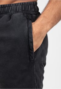 Zwarte joggerbroeken met een elastische tailleband en zijzak. Zachte stof met een gladde textuur en zichtbare stiksels.