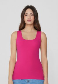 Top ajustado sin mangas en un brillante color rosa, con escote cuadrado y tejido suave. Combinado con jeans de mezclilla azul claro.