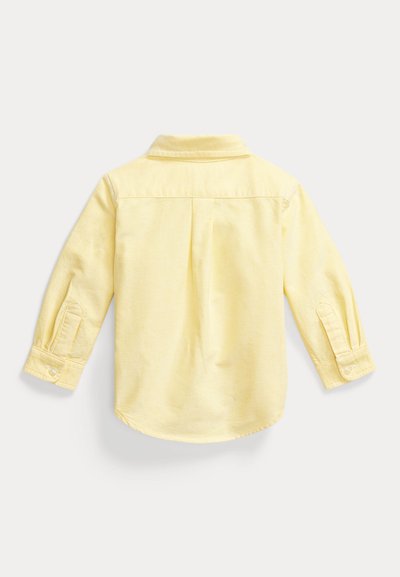 Ανοιχτό κίτρινο παιδικό μακρυμάνικο πουκάμισο με μανσέτες με κουμπιά, πίσω καβάλο και κεντρικό πιέτα, απλωμένο επίπεδα σε λευκό φόντο.