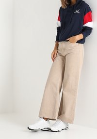 Marinblå hoodies med röda och vita detaljer, beige vida byxor och vita sneakers med svarta sulor. Avslappnad outfit med lös passform.