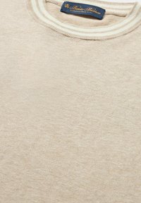 Bežový pletený svetr s texturovaným povrchem a žebrovaným krémovým límcem. Štítek s modrým šitím viditelný na dekoltu.