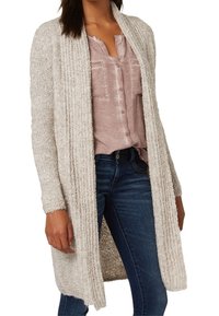 Knit cardigan in light beige, open front design, long sleeves with ribbed texture, worn over a pink button-up top and blue jeans.