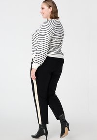 Gestreepte trui in wit en zwart met pofmouwen, gecombineerd met zwarte broeken met een crèmekleurige zijstreep en zwarte laarzen met hak.