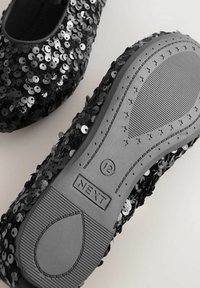 Bailarinas negras con lentejuelas, con punta redondeada, parte superior texturizada cubierta de brillantes lentejuelas negras y plateadas, con una suela de goma gris con patrones de agarre.
