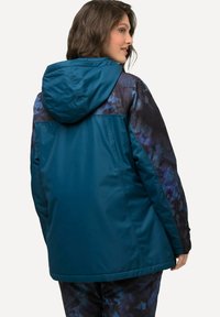 Giacca teal con cappuccio, caratterizzata da un motivo astratto blu scuro e nero sulle spalle e sulle maniche, realizzata in materiale liscio e leggero.
