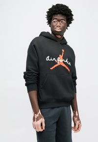 Μαύρο φούτερ με κουκούλα, με μεγάλο πορτοκαλί και λευκό λογότυπο Air Jordan. Διαθέτει τσέπη μπροστά και ριμπ μανσέτες. Υλικό από υφή βαμβακιού.