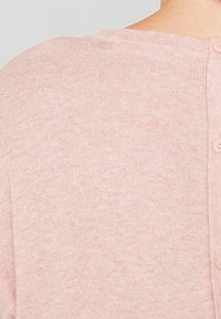 Valkoinen vaaleanpunainen neulecardigan, jossa on pyöreä kaula-aukko, teksturoitu pinta ja kuusi yhteensopivaa nappia takasaumassa.