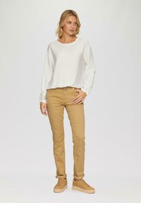 Witte lange mouwen top van textuurstof, gecombineerd met beige slim-fit broek en lichtbruine sneakers op een effen achtergrond.