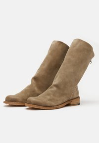 Bottes en daim jusqu'aux genoux dans une teinte marron clair. Texture lisse, bout arrondi et talon empilé. Présente un subtil détail de fermeture éclair à l'arrière.
