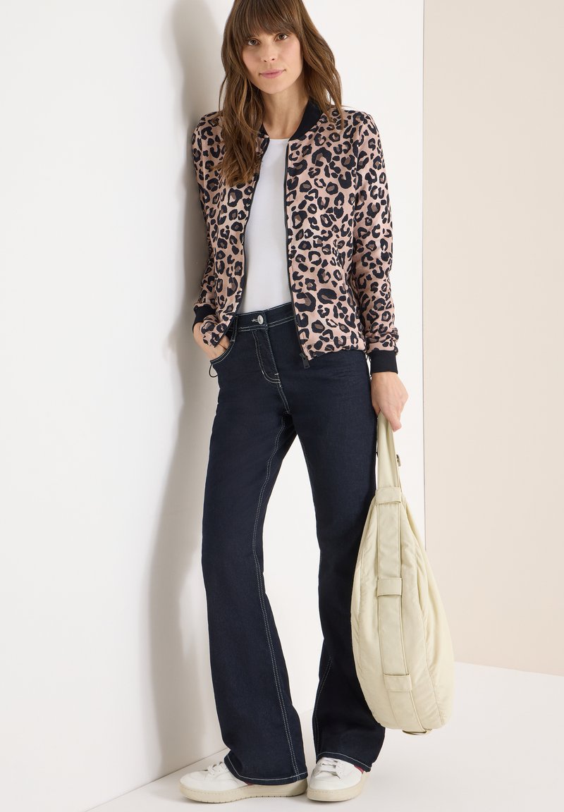 Bomberjack met luipaardprint in roze en zwart, gecombineerd met donkerblauwe uitlopende jeans. Witte T-shirt en een crèmekleurige tas maken de look compleet.