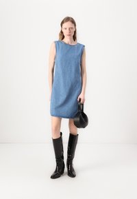 Denim bez piedurknēm kleita ar brīvu piegriezumu, gaiši zila krāsa un neapstrādāta apakšmala. Apvienota ar melniem spīdīgiem zābakiem līdz ceļiem un mazu melnu somu.