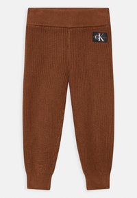 Leggings de punto marrón con una cinturilla acanalada. Tejido texturizado con un diseño de punto ajustado. Cuenta con un parche de logo visible en la parte trasera.