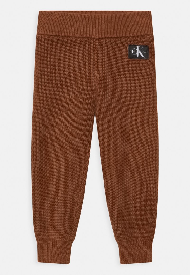 Leggings de punto marrón con una cinturilla acanalada. Tejido texturizado con un diseño de punto ajustado. Cuenta con un parche de logo visible en la parte trasera.