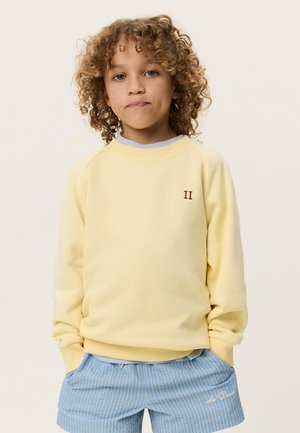 Hellgelbes Sweatshirt mit rundem Ausschnitt und langen Ärmeln. Verfügt über ein kleines rotes "II" auf der Brust. Weicher, strukturierter Stoff.