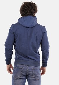 Felpa blu navy realizzata in morbido cotone misto, con cappuccio regolabile, polsini a costine e vita aderente, vista da dietro.