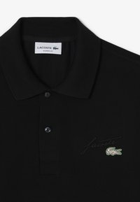 Czarna koszulka polo z teksturowanej tkaniny, z klasycznym kołnierzykiem, trzema czarnymi guzikami i zielonym haftowanym logo Lacoste.