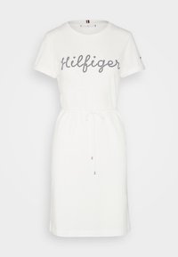 White cotton dress with short sleeves, drawstring waist, and "Hilfiger" in navy rhinestones on the front. Smooth texture and casual design.