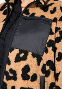 Hnědá a černá leopardí potisková fleecová bunda s hladkým černým zipovým prsním kapsou a kontrastním černým materiálem na límci a vpředu.