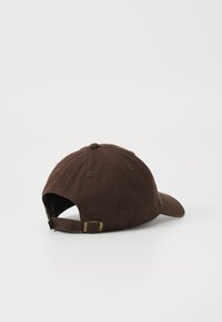 Cappellino da baseball in cotone marrone con visiera curva, cinturino regolabile con dettagli in oro e finitura testurizzata sul tessuto.