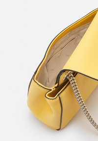 Borsa a mano in pelle gialla con superficie testurizzata, dotata di tracolla a catena, bordatura a contrasto e interno beige con dettaglio logo.