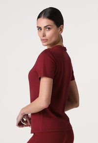 T-shirt bordeaux a maniche corte realizzato in tessuto morbido, con colletto tondo e design aderente. Texture liscia con cuciture minime.