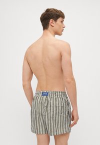 Gestreifte Badeshorts in Oliv und Weiß, mit einem elastischen Bund, einer aufgesetzten Tasche auf der Rückseite und einem Markenetikett.
